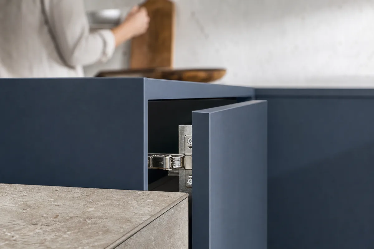 Détail de quincaillerie inox et de façade bleu ardoise sur un meuble de cuisine sablais éclairé par la lumière atlantique